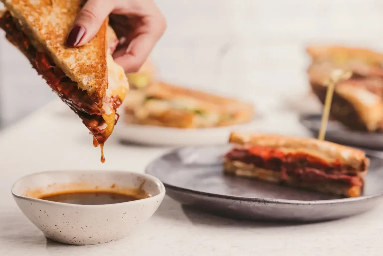 Hand dipping a grilled sandwich into a bowl of sauce