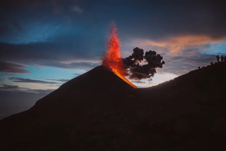 Volcán de Fuego erupting against a blue hour sky with hikers silhouetted on the ridge, Guatemala