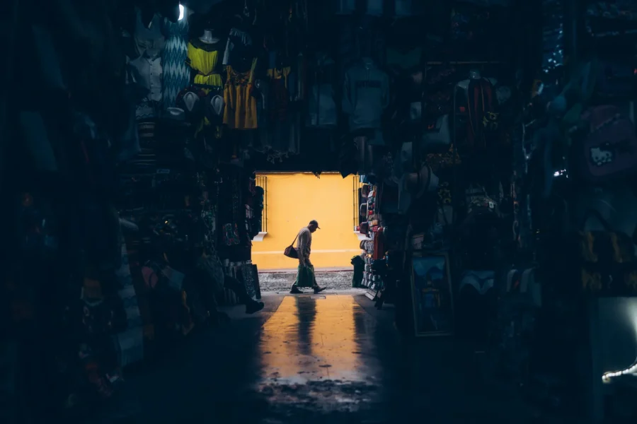 Looking out through a market shop stocked floor to ceiling in Antigua Guatemala to a man crossing a bright yellow wall outside
