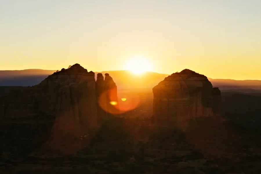 Telephoto aerial silhouette of Cathedral Rock in Sedona, Arizona with the setting sun between its spires and warm lens flare.