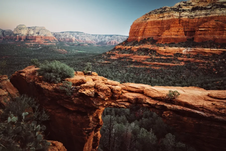 Devil's Bridge natural sandstone arch in Sedona, Arizona just before sunrise, glowing orange above a green valley with pale cliffs in the distance.
